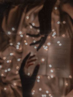 a woman's hand reaching out from behind a curtain with lights on the wall