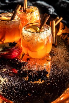 two glasses filled with drinks sitting on top of a metal tray next to cinnamon sticks