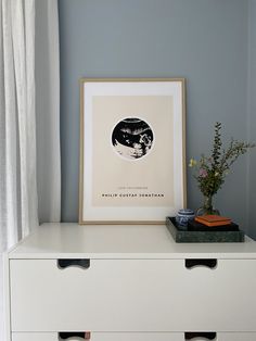 a white dresser with two drawers and a framed print