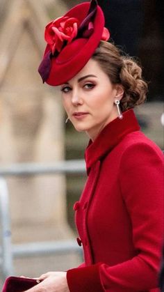 a woman wearing a red coat and hat with a flower on it's head