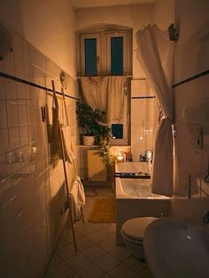 a dimly lit bathroom with two toilets and a bathtub in the corner, next to a window