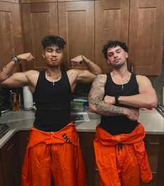 two men standing in a kitchen with their arms crossed and one is showing off his muscles