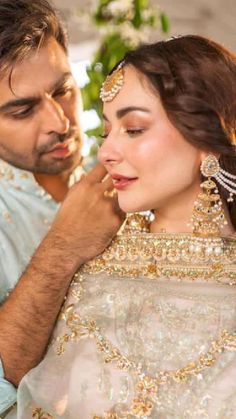 a man fixing the ear of a woman in a wedding dress with gold jewelry on her head