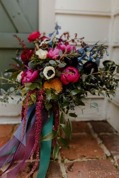 a bouquet of flowers sitting on top of a brick floor next to a door with green ribbon