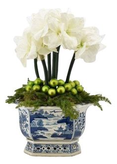 white flowers in a blue and white vase filled with green balls, grass and greenery