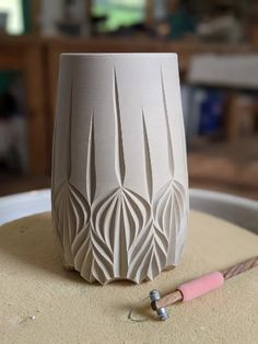 a white vase sitting on top of a table next to a pink pen and pencil