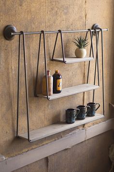 a shelf with three shelves and two cups on it next to a potted plant