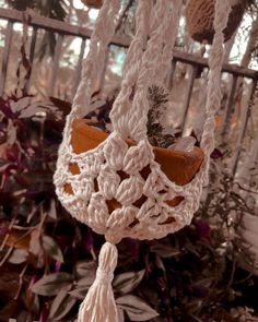 a white crocheted hanging planter in front of some plants