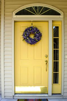 a yellow front door with a wreath on it and a welcome mat in front of it