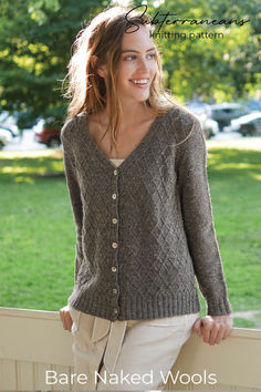 a woman wearing a brown sweater and tan pants standing next to a fence with her hands on her hips