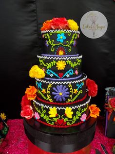 a multi - tiered cake with colorful flowers on the top and bottom is decorated with black ribbon