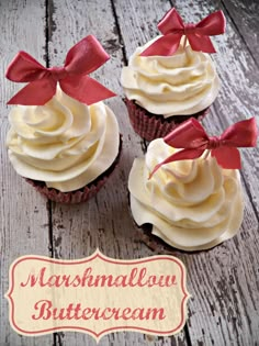 three cupcakes with white frosting and red bows on top are sitting on a wooden table