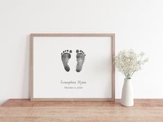 a white vase sitting next to a wooden table with a baby's foot print on it