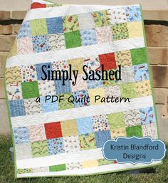 a quilted blanket sitting on top of grass next to a brick wall with the words simply sashed