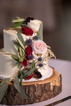 a wedding cake with flowers and greenery on a tree stump at the reception table