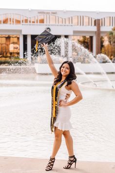 a woman is posing in front of a fountain with her graduation cap up in the air