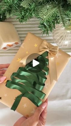 someone holding a wrapped present in front of a christmas tree ornament with green ribbon