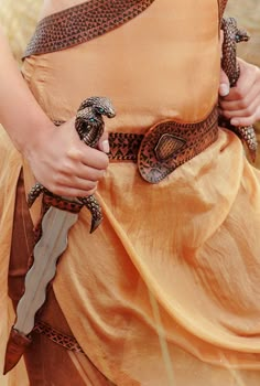 a woman in an orange dress holding a snake wrapped around her waist and wearing a brown belt