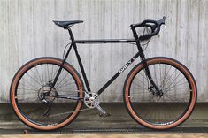 a black bike with orange rims parked next to a wooden wall on the sidewalk