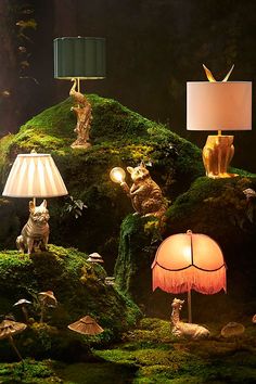 an assortment of lamps and figurines on display in a mossy forest setting