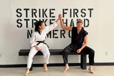 two people sitting on a bench in front of a wall that says strike first, strike hard, never forget