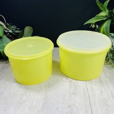 two yellow plastic containers sitting next to each other on a white table with plants in the background