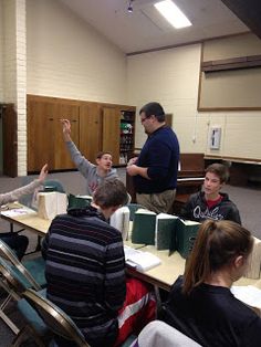 a group of people sitting around a table with boxes on it and one person raising his hand