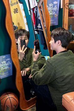 two young men sitting in front of a mirror looking at their cell phones and taking pictures