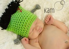 a newborn baby wearing a green crochet hat with black pom - poms