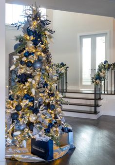 a decorated christmas tree with blue and gold ornaments in a living room next to stairs