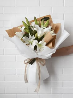 a bouquet of white lilies wrapped in brown paper and tied to a brick wall