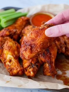 a hand is pointing at some chicken wings