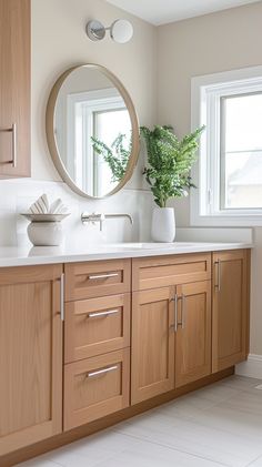 a bathroom with wooden cabinets and a round mirror on the wall above the sink is a potted plant