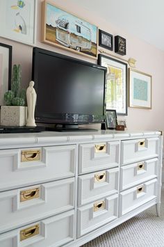 a flat screen tv sitting on top of a white dresser next to pictures and vases