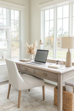 a laptop computer sitting on top of a wooden desk in front of two large windows