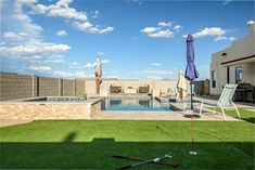 an empty pool with lawn chairs and umbrellas next to it on the grass in front of a house