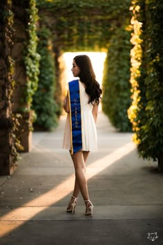 a woman wearing a blue and white sash standing on a sidewalk in front of an archway