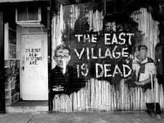 the east village is dead sign painted on a wall with two men's faces