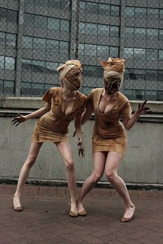 two women dressed in costumes standing next to each other on a brick floor near a building