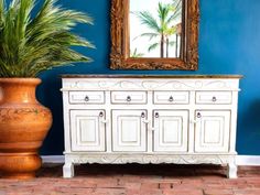 a white dresser sitting next to a potted plant on top of a brick floor