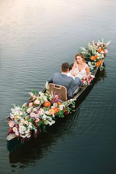 a bride and groom are sitting in a boat with flowers on the front, surrounded by greenery