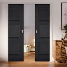 two black doors are open in a room with hardwood floors and white walls, along with a wicker basket on the floor