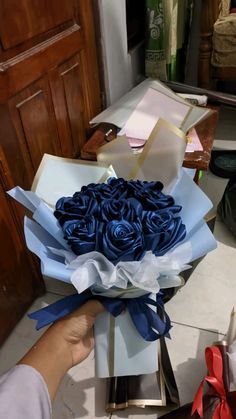 a person holding a bouquet of blue roses in a box on the floor next to other boxes