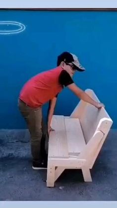 a man in red shirt and black hat standing next to a white bench with one foot on it