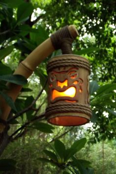 a lantern hanging from a tree in the woods with leaves around it and a pumpkin carved on top