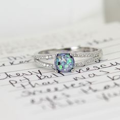 a white gold ring with an opal and diamond set in the middle on top of a sheet of paper