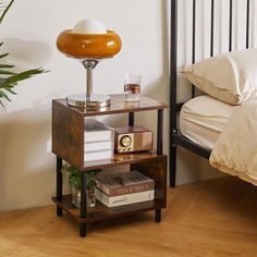 a small wooden shelf with books on it in front of a bed and a potted plant