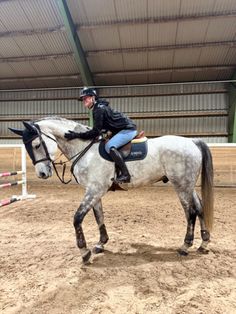 a woman riding on the back of a white horse in an indoor arena with dirt flooring