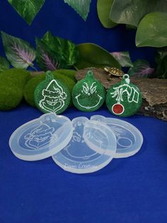 three plastic discs with stickers on them sitting next to some green plants and leaves