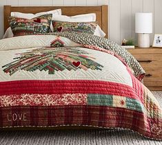 a bed with red and green quilts on it in a room next to a dresser